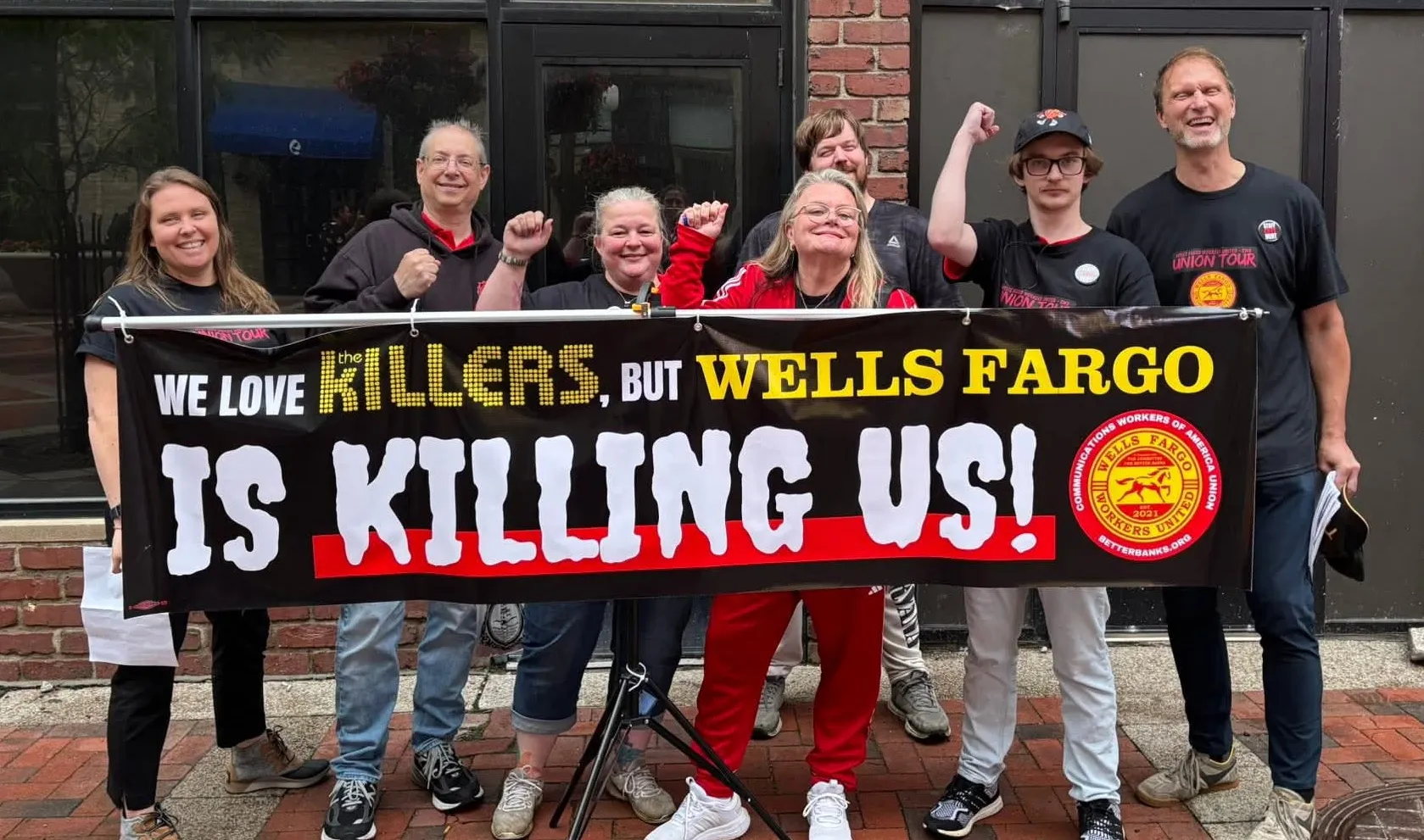 Wells Fargo Workers United members hold banner reading "we love The Killers, but Wells Fargo is Killing us! 
